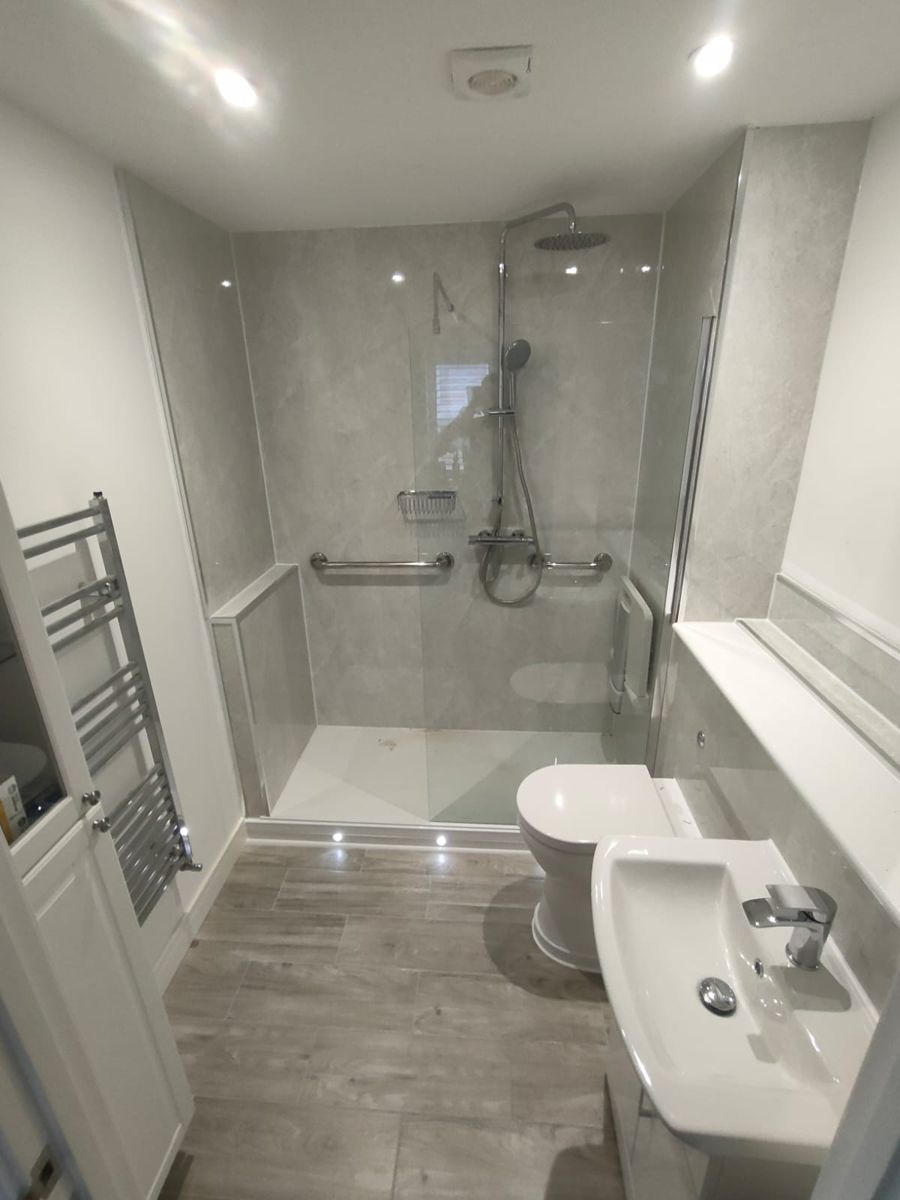 After: whole room with walk-in shower, marble-effect wall panelling, grab rails, folding seat, toilet and vanity basin